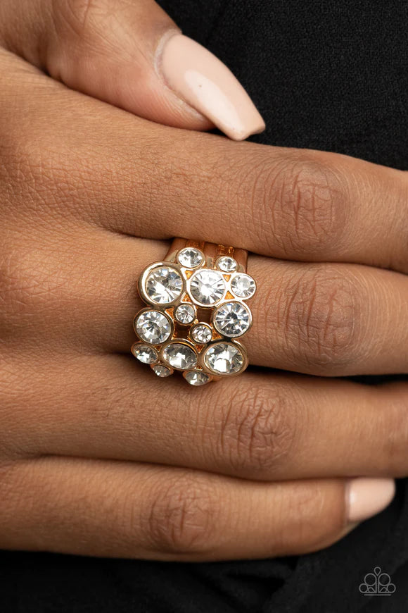 Paparazzi Accessories Bubbling Bravado - Gold Encased in sleek gold frames, a bubbly collection of sparkly white rhinestones coalesces into a glamorous band across the finger. Features a stretchy band for a flexible fit. Sold as one individual ring. Jewel