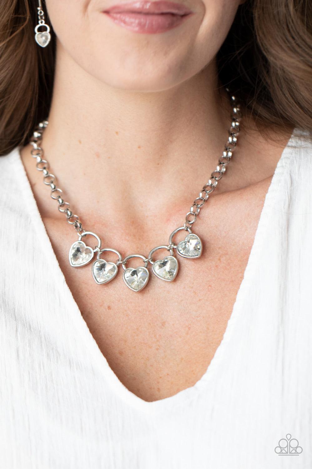 Paparazzi Accessories HEART on Your Heels - White Dotted with glittery white heart-shape gems, shimmery silver locket-like frames link together at the bottom of an exaggerated silver chain, creating a sparkling statement piece below the collar. Features a