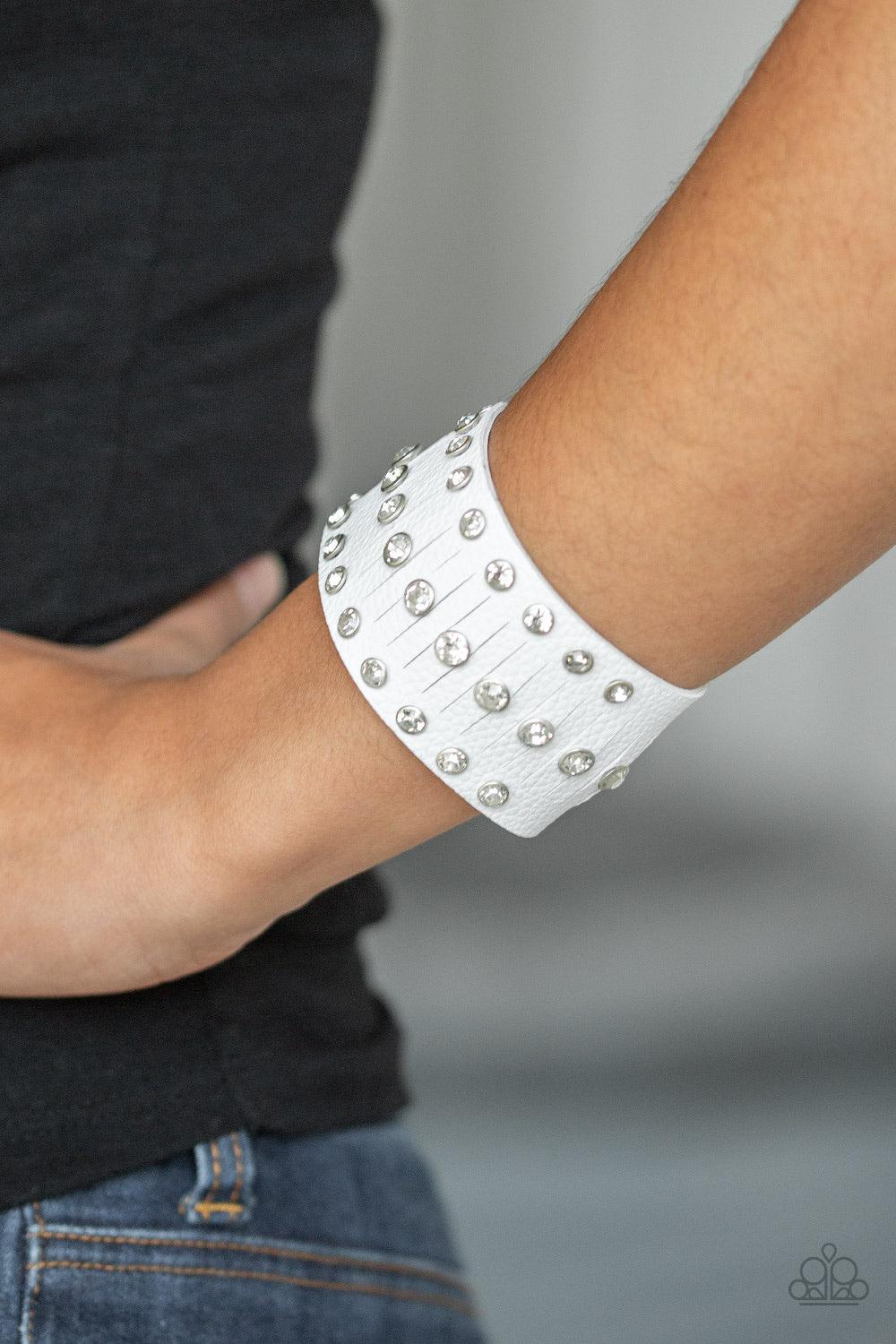 Paparazzi Accessories Now Taking The Stage - White Pressed into sleek silver frames, glittery white rhinestones are studded across a thick white leather band featuring a center lined with slits for a sassy finish. Features an adjustable snap closure. Jewe