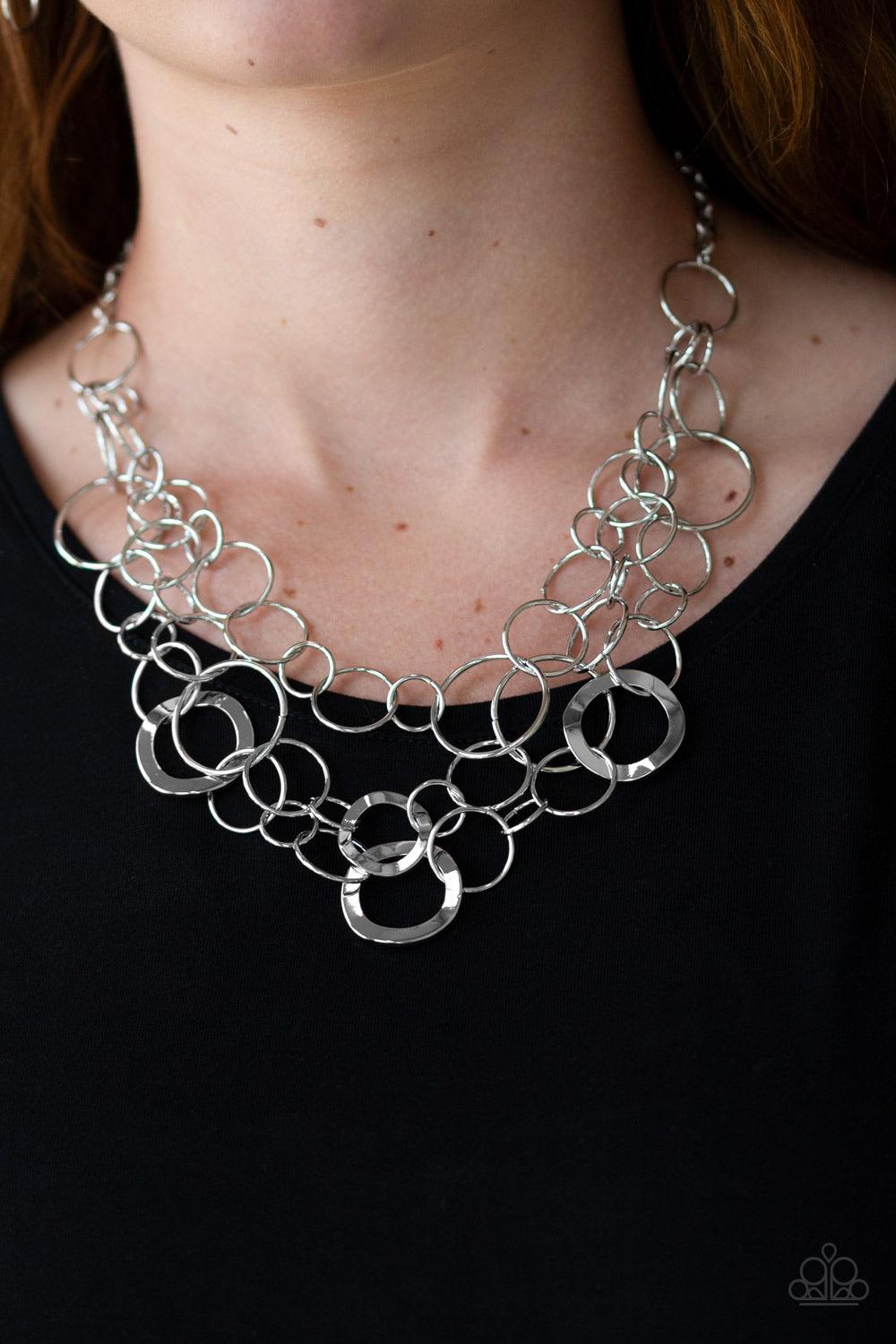 Paparazzi Accessories Main Street Mechanics - Silver Featuring beveled and smooth surfaces, mismatched silver rings link below the collar in three glistening layers for a gritty look. Features an adjustable clasp closure. Sold as one individual necklace.