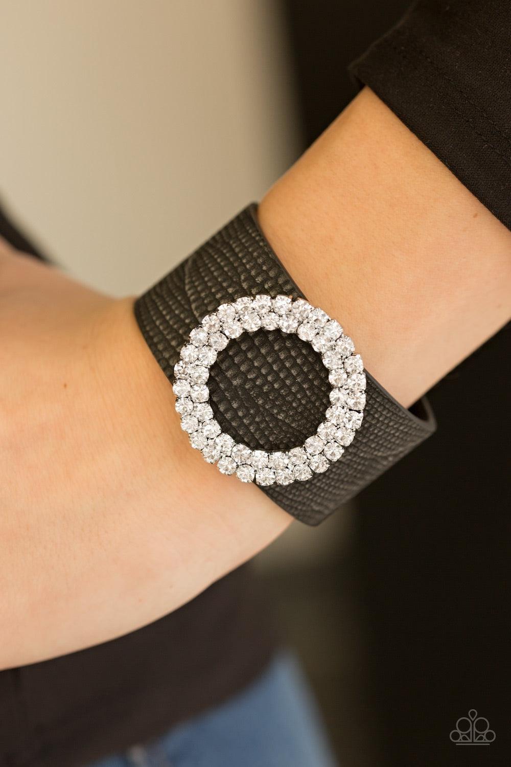 Paparazzi Accessories Ring In The Bling - Black Encrusted in glittery white rhinestones, a round frame slides along a rustic strip of black leather for a fierce look. Features an adjustable snap closure. Jewelry