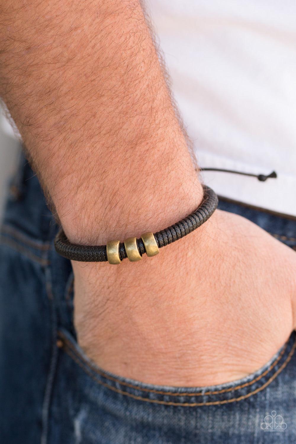 Paparazzi Accessories One For The Trail - Brass Shiny black twine wraps around a black cord, creating an urban look around the wrist. Shiny brass beads slide along the cording for a rugged finish. Features an adjustable sliding knot closure. Jewelry