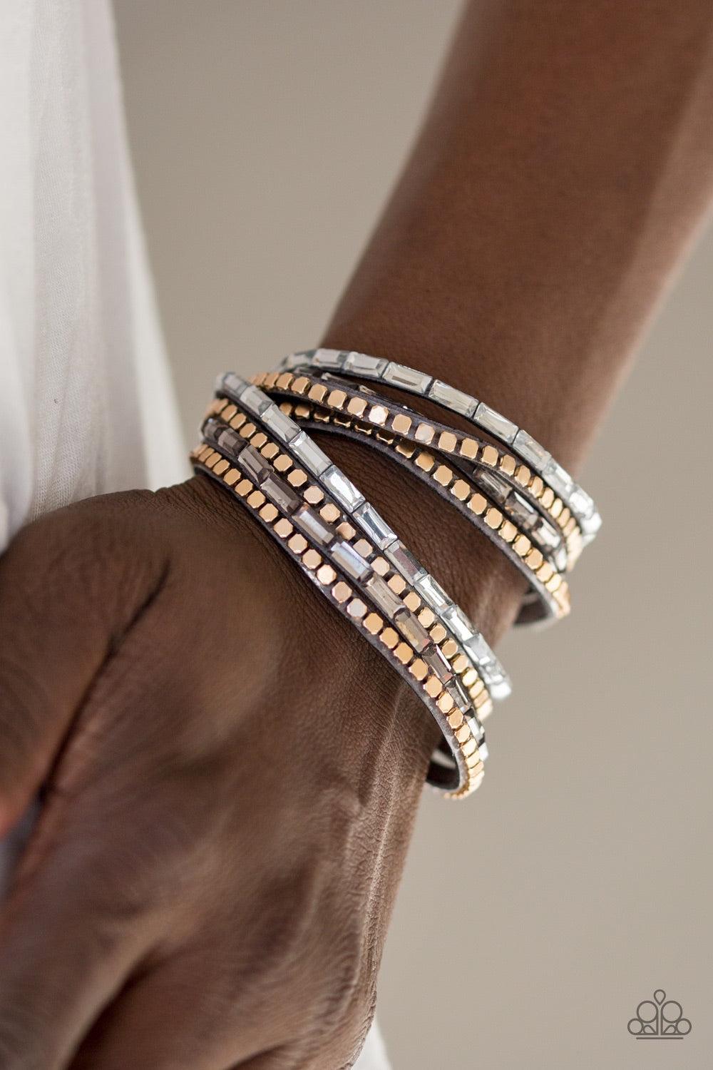 Paparazzi Accessories This Time With Attitude - Silver Smoky and white emerald cut rhinestones and flat gold cube beads are encrusted along strands of gray suede for a sassy look. The elongated band double wraps around the wrist for a fierce one-of-a-kind