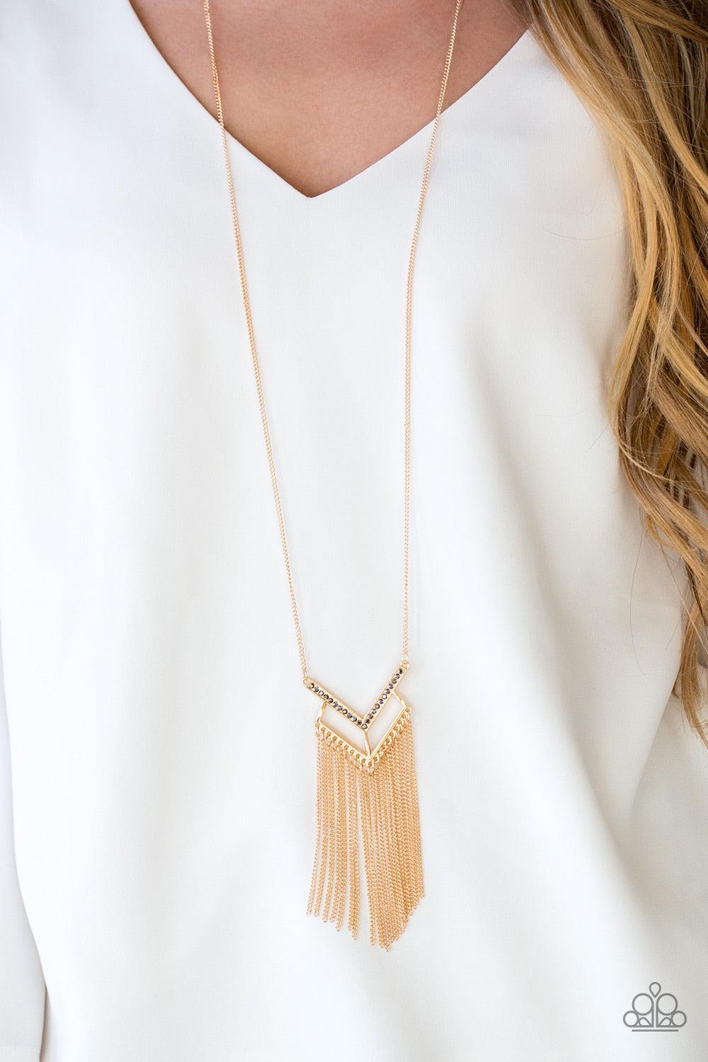 Paparazzi Accessories Alpha Glam - Gold Encrusted in hematite rhinestones, a V-shaped frame attaches to an airy gold frame, creating a stacked pendant. Swinging from the bottom of a lengthened gold chain, the glamorous pendant gives way to a tapered fring