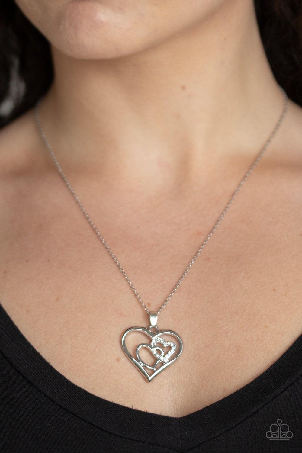 Paparazzi Accessories Cupid Charm - White A white rhinestone encrusted heart intertwines with a plain silver heart inside of a larger silver heart frame, creating a romantic pendant at the bottom of a shimmery silver chain. Features an adjustable clasp cl