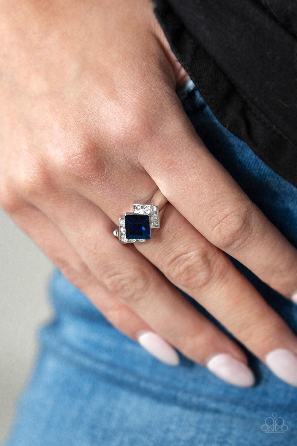 Paparazzi Accessories Wall Street Winner - Blue Featuring a regal square cut, a glittery blue rhinestone sits atop a bold silver band dusted in sparkling white rhinestones for a refined flair. Features a dainty stretchy band for a flexible fit. Jewelry