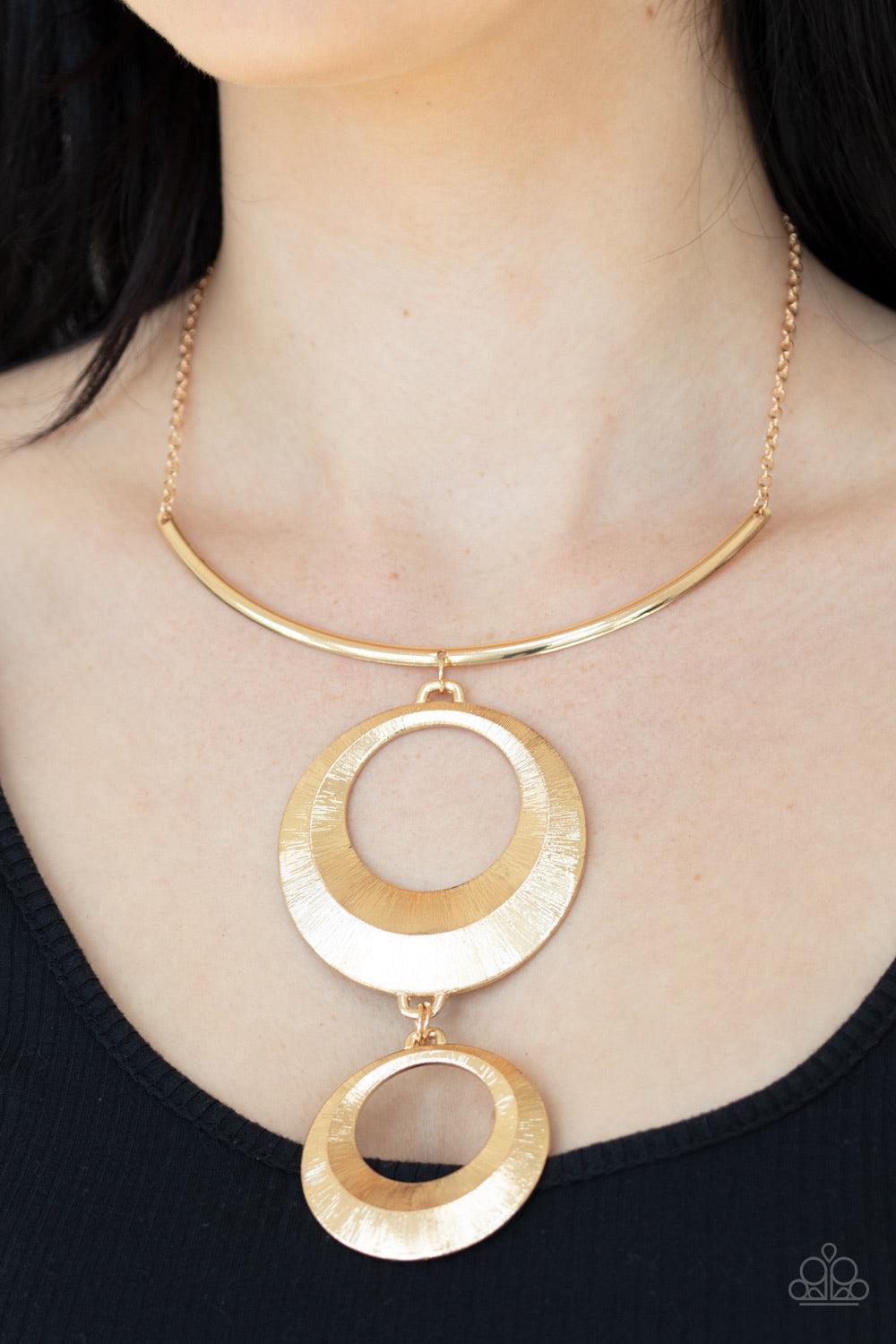 Paparazzi Accessories Egyptian Eclipse - Gold Featuring a blinding scratch finish, two beveled gold circular frames swing from the bottom of a bowing gold rod, creating an edgy stacked pendant down the chest. Features an adjustable clasp closure. Jewelry