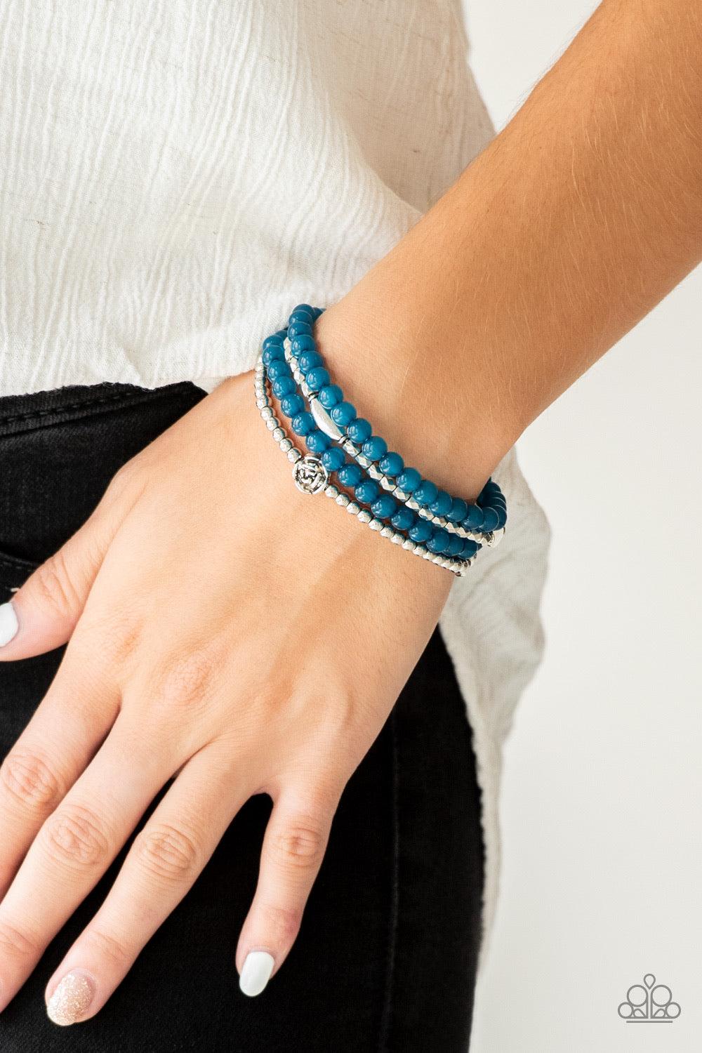 Paparazzi Accessories Blooming Buttercups - Blue Mismatched silver beads and strands of glassy blue beads are threaded along stretchy bands. Infused with silver accents, dainty rose blossoms adorn the wrist for a seasonal finish. Sold as one set of four b