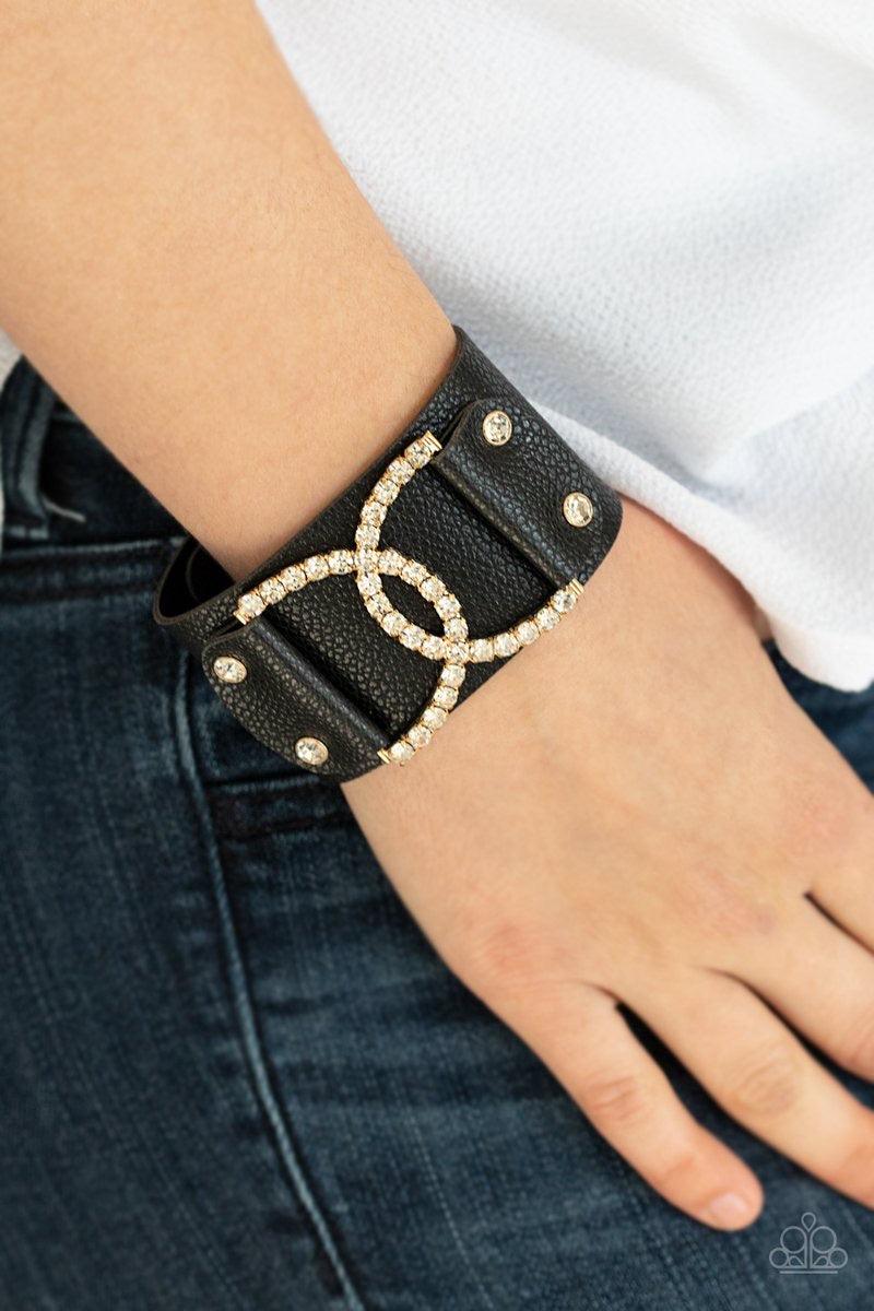 Paparazzi Accessories Couture Culture - Gold Encrusted in glassy white rhinestones, two interlocking half moon gold frames are studded in place across the front of a black leather band for a statement-making finish. Features an adjustable snap closure. So