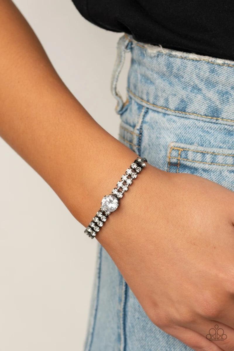 Paparazzi Accessories Gorgeously Glitzy - Black An oversized white rhinestone dots the center of two rows of glittery white rhinestones that attach to a dainty strand of gunmetal box chain around the wrist for a glamorous finish. Features an adjustable sl