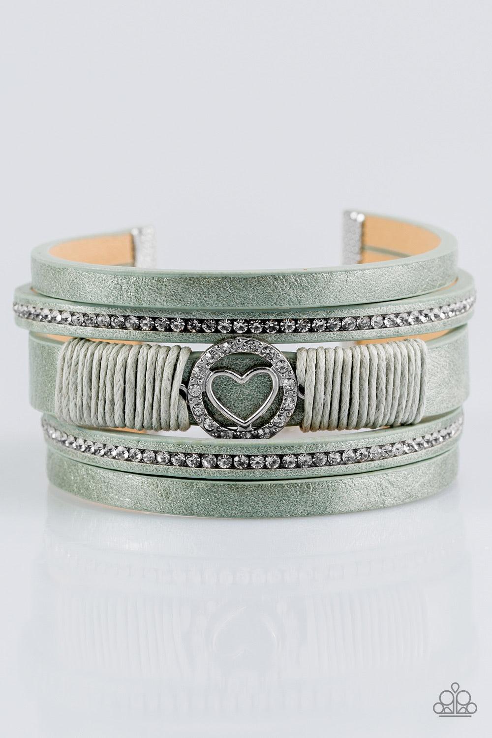 Paparazzi Accessories It Takes Heart - Green Brushed in a metallic shimmer, strips of green leather are encrusted in alternating rows of glittery white rhinestones. Green cording knots around the centermost strand, securing a sparkling heart frame in plac