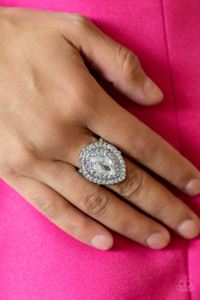 Paparazzi Accessories Icy Indulgence - White A dramatically oversized white teardrop gem twinkles inside two borders of glassy white rhinestones, resulting in a sparkly statement atop the finger. Features a stretchy band for a flexible fit. Sold as one in