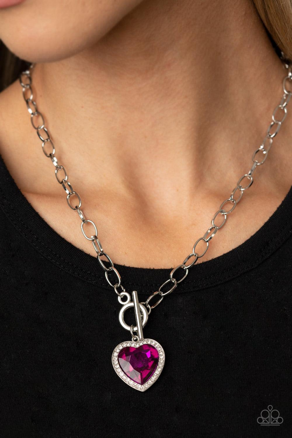 Paparazzi Accessories Check Your Heart Rate - Pink Bordered in glassy white rhinestones, a heart-shaped Pink Peacock gem is pressed into a shiny silver pendant at the bottom of a bold silver chain below the collar for a flirtatious finish. Features a togg