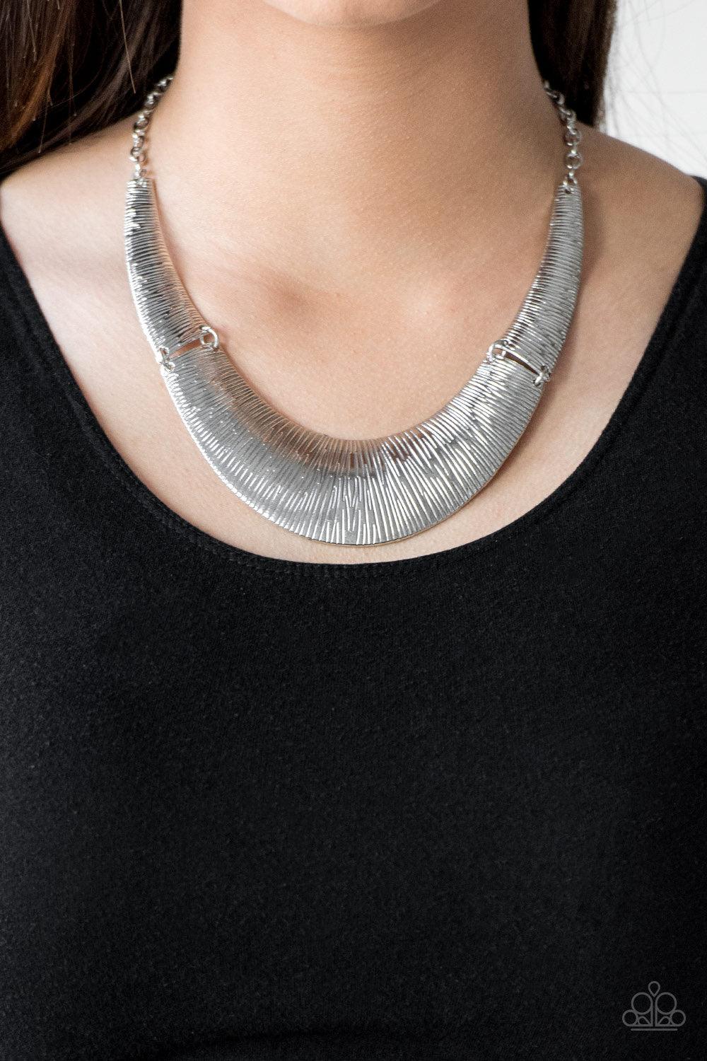 Paparazzi Accessories Feast or Famine - Silver Etched in linear patterns, dramatic silver plates connect below the collar, joining into a fierce crescent-shaped pendant for a statement making look. Features an adjustable clasp closure. Sold as one individ