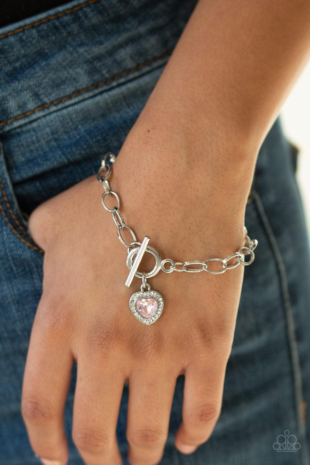 Paparazzi Accessories Going Steady - Pink Featuring a pink heart-shaped rhinestone center, a glittery white rhinestone encrusted silver frame swings from a shimmery silver chain for a flirtatious fashion. Features a toggle closure. Jewelry