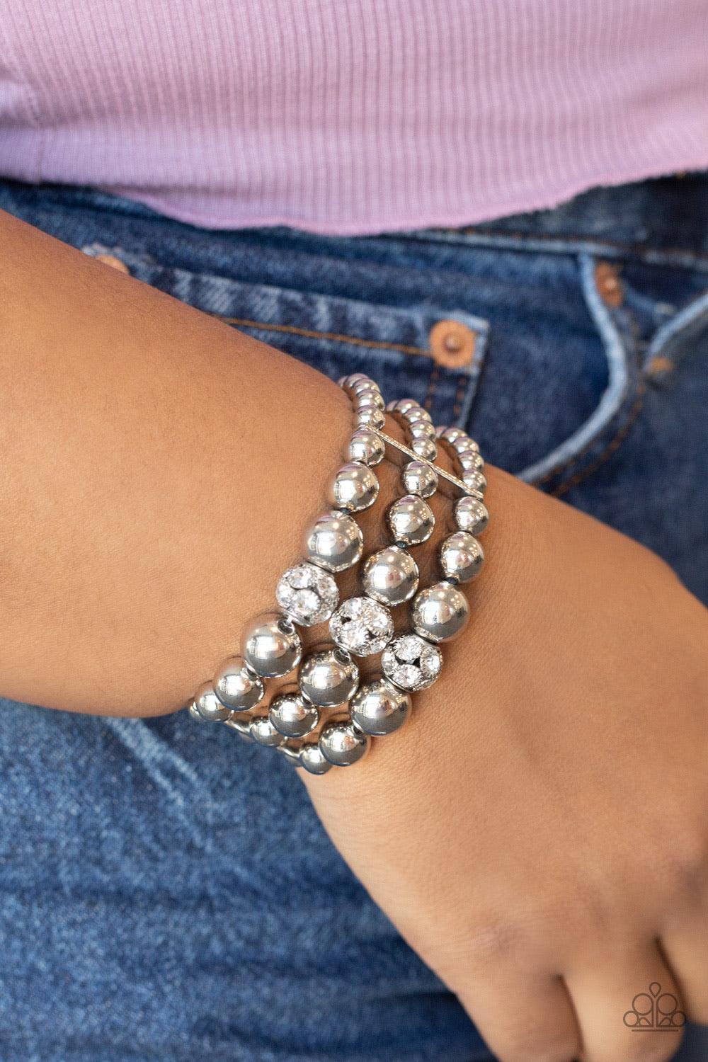 Paparazzi Accessories Icing On The Top - White Held together with dainty silver fittings, strands of silver beads are threaded along stretchy bands around the wrist. Glassy white rhinestone encrusted beads adorn the center, adding a splash of sparkle to t
