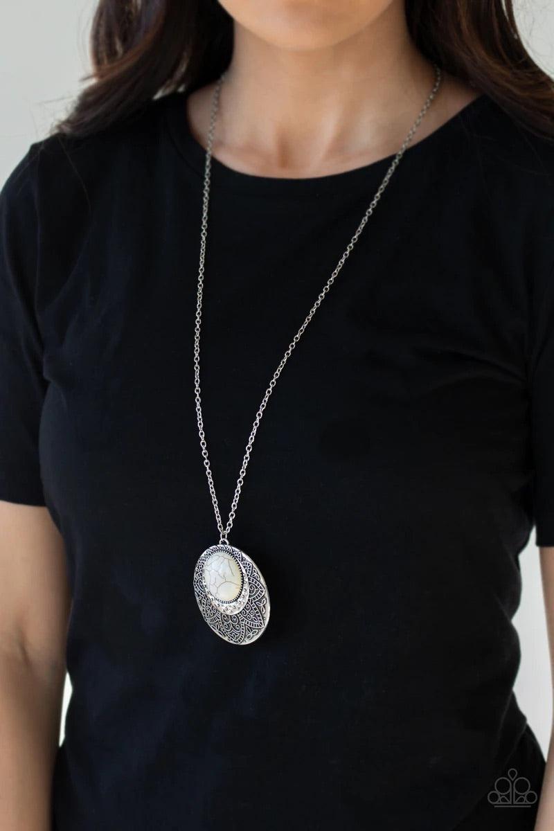 Paparazzi Accessories Medallion Meadow - White Swinging from the bottom of a lengthened silver chain, a refreshing white stone is pressed into a hammered silver medallion radiating with floral details for a bold tribal inspired look. Features an adjustabl