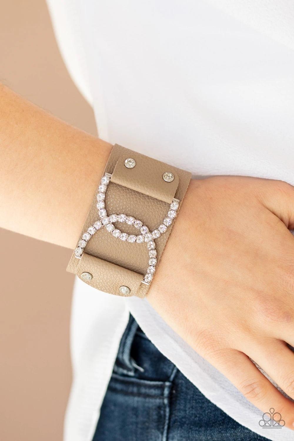 Paparazzi Accessories Couture Culture - Brown Encrusted in glassy white rhinestones, two interlocking half moon silver frames are studded in place across the front of a brown leather band for a statement-making finish. Features an adjustable snap closure.