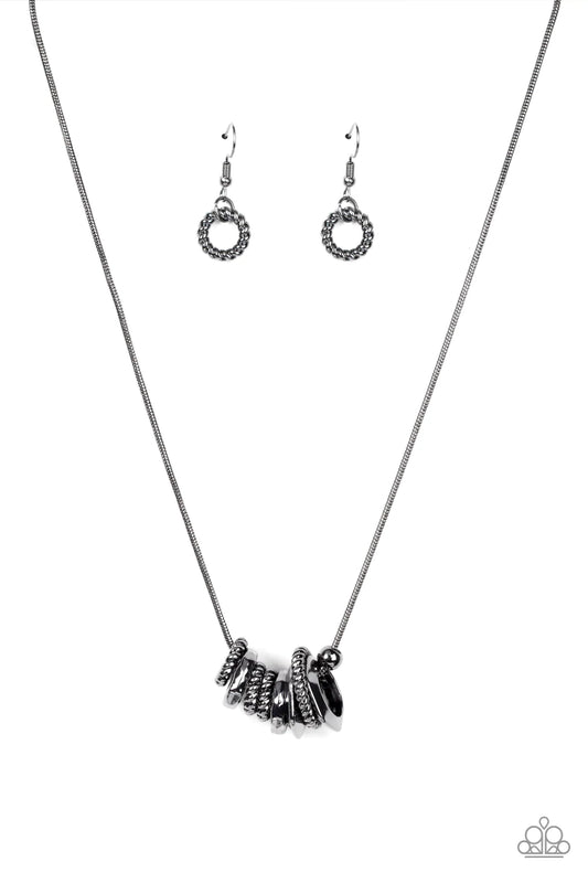 Paparazzi Accessories Mechanically Mischief - Black A gritty assortment of gunmetal ropelike rings, hammered gunmetal rings, and faceted gunmetal rings glide along a rounded gunmetal snake chain, creating an intense industrial collar below the collar. Fea