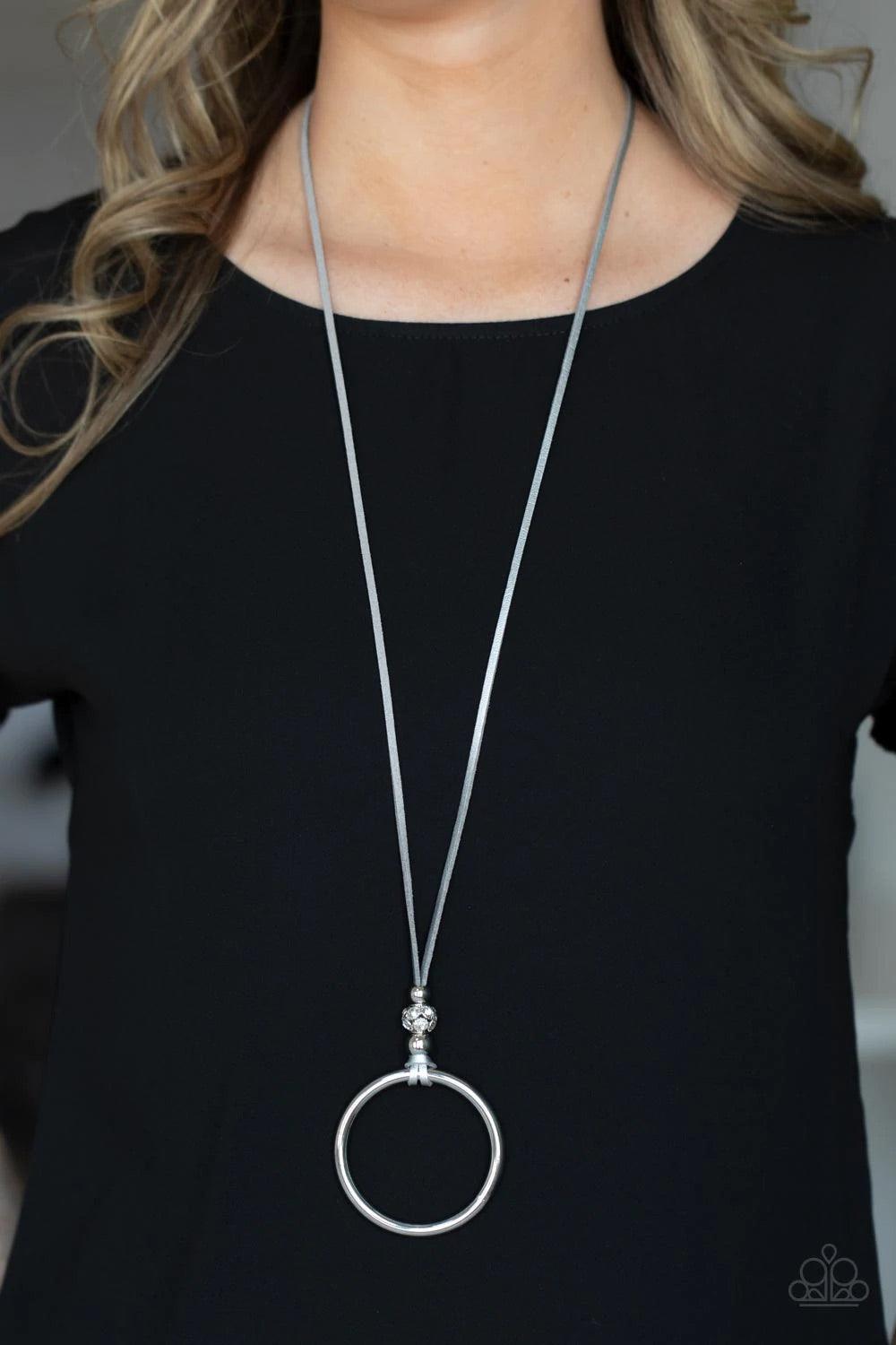 Paparazzi Accessories BLING Into Focus - Silver Infused with a pair of classic silver beads and a white rhinestone encrusted accent, lengthened shimmery silver leather cording knots around a bold silver hoop for a knockout look. Features an adjustable cla