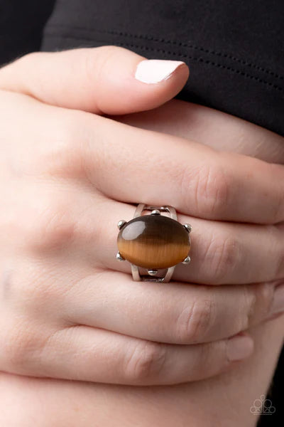 Paparazzi Accessories Enchantingly Everglades - Brown An oval brown cat's eye gemstone sits atop a pronged silver frame along two layered silver bands, resulting in an enchanting centerpiece atop the finger. Features a stretchy band for a flexible fit. So