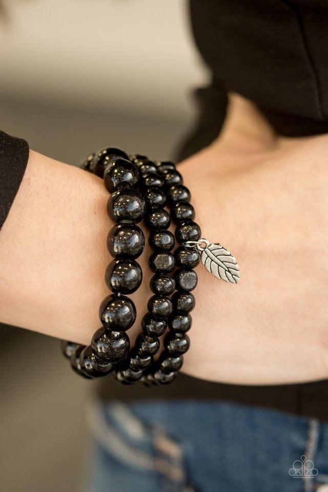 Paparazzi Accessories Out of the Woods - Black Painted in a neutral black finish, wooden beads are threaded along three elastic bands. A shimmery silver leaf charm swings from the wrist, adding a wanderlust finish to the seasonal look. Sold as one set of