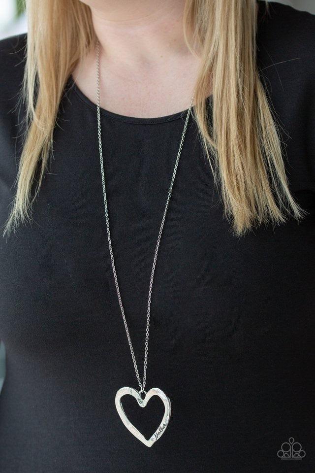 Paparazzi Accessories A Mother’s Love - Silver Swinging from the bottom of a lengthened silver chain, an asymmetrical heart pendant is stamped in the word, "mom" and dotted with a single white rhinestone for a whimsical look. Features an adjustable clasp