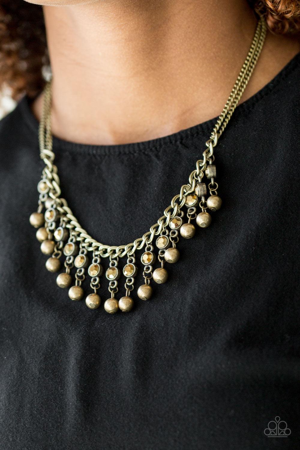 Paparazzi Accessories Pageant Queen - Brass Sparkling aurum rhinestones drip from the bottom of a bold brass chain. Classic brass beads swing from the bottoms of the glittery rhinestones, creating a glamorous fringe below the collar. Features an adjustabl