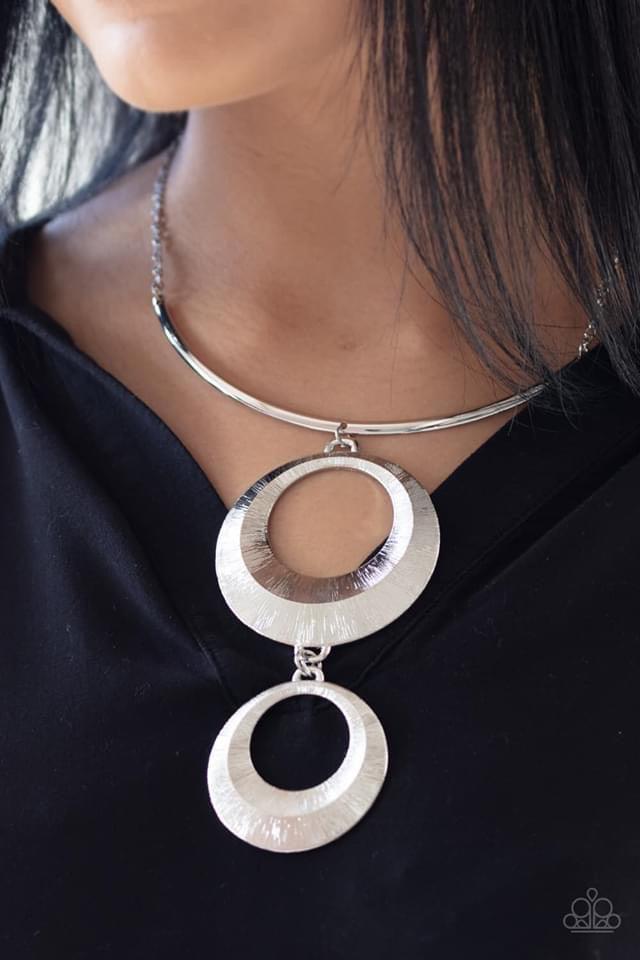 Paparazzi Accessories Egyptian Eclipse - Silver Featuring a blinding scratch finish, two beveled silver circular frames swing from the bottom of a bowing silver rod, creating an edgy stacked pendant down the chest. Features an adjustable clasp closure. Je