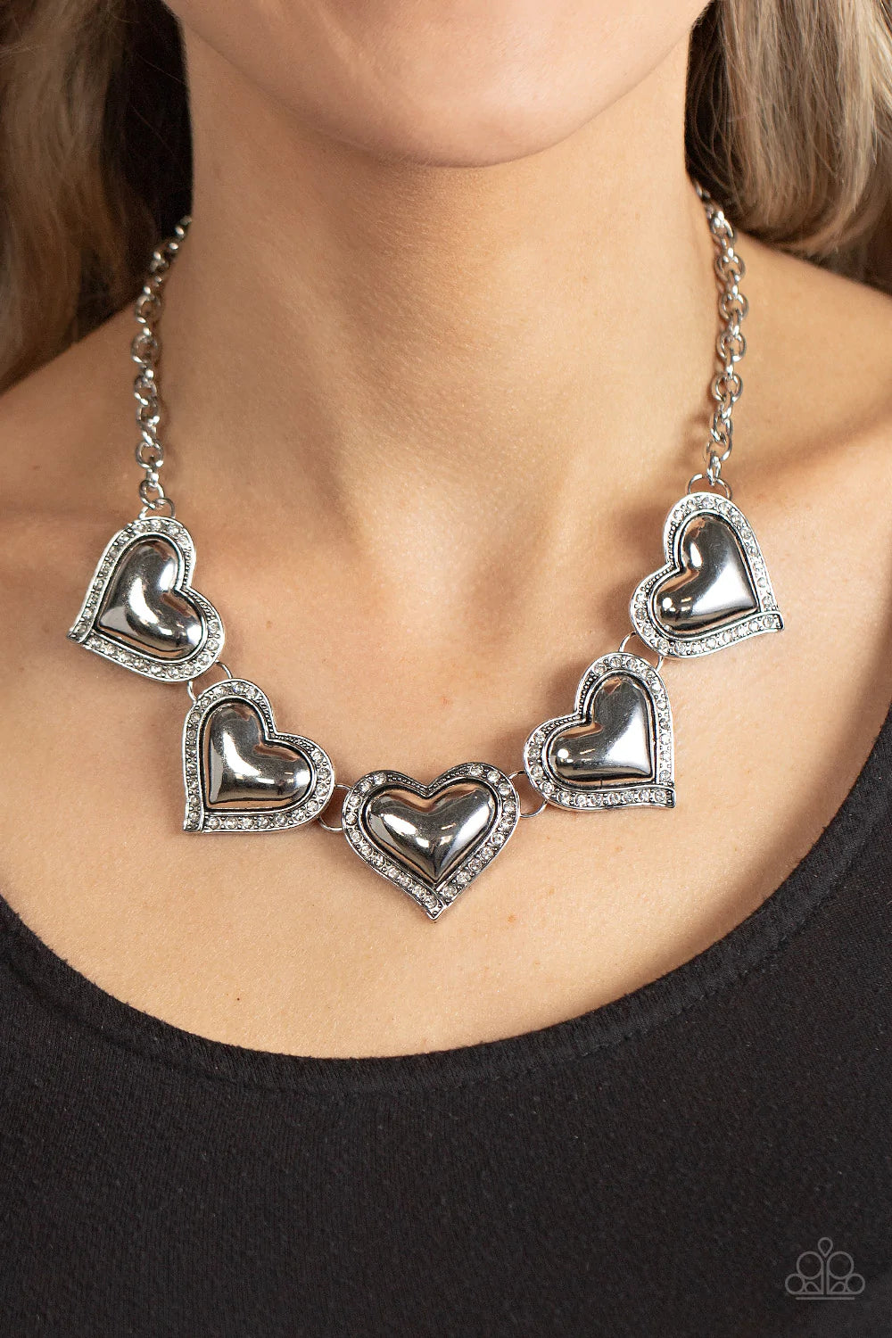 Paparazzi Accessories Kindred Hearts - White Bordered in glitzy hematite rhinestones, an oversized collection of beveled silver heart frames delicately links below the collar for a dramatically romantic look. Features an adjustable clasp closure. Sold as