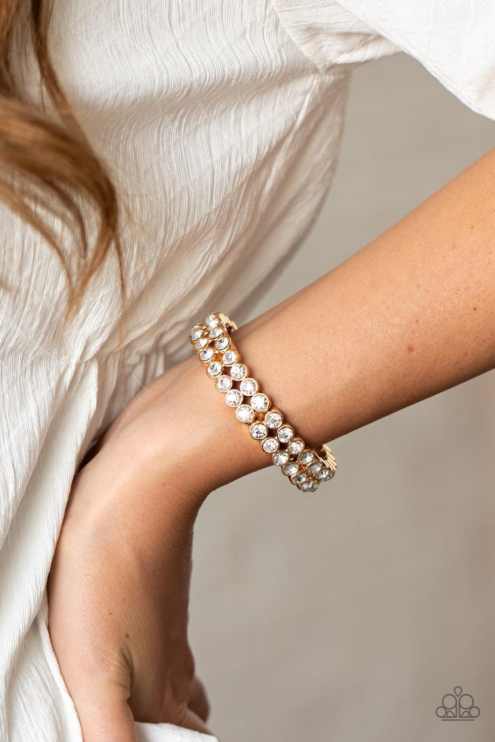 Paparazzi Accessories Come And Get It! - Gold Pairs of glittery white rhinestones stack into sections of blinding frames that have been threaded along a stretchy band around the wrist for a glamorous look. Sold as one individual bracelet. Jewelry