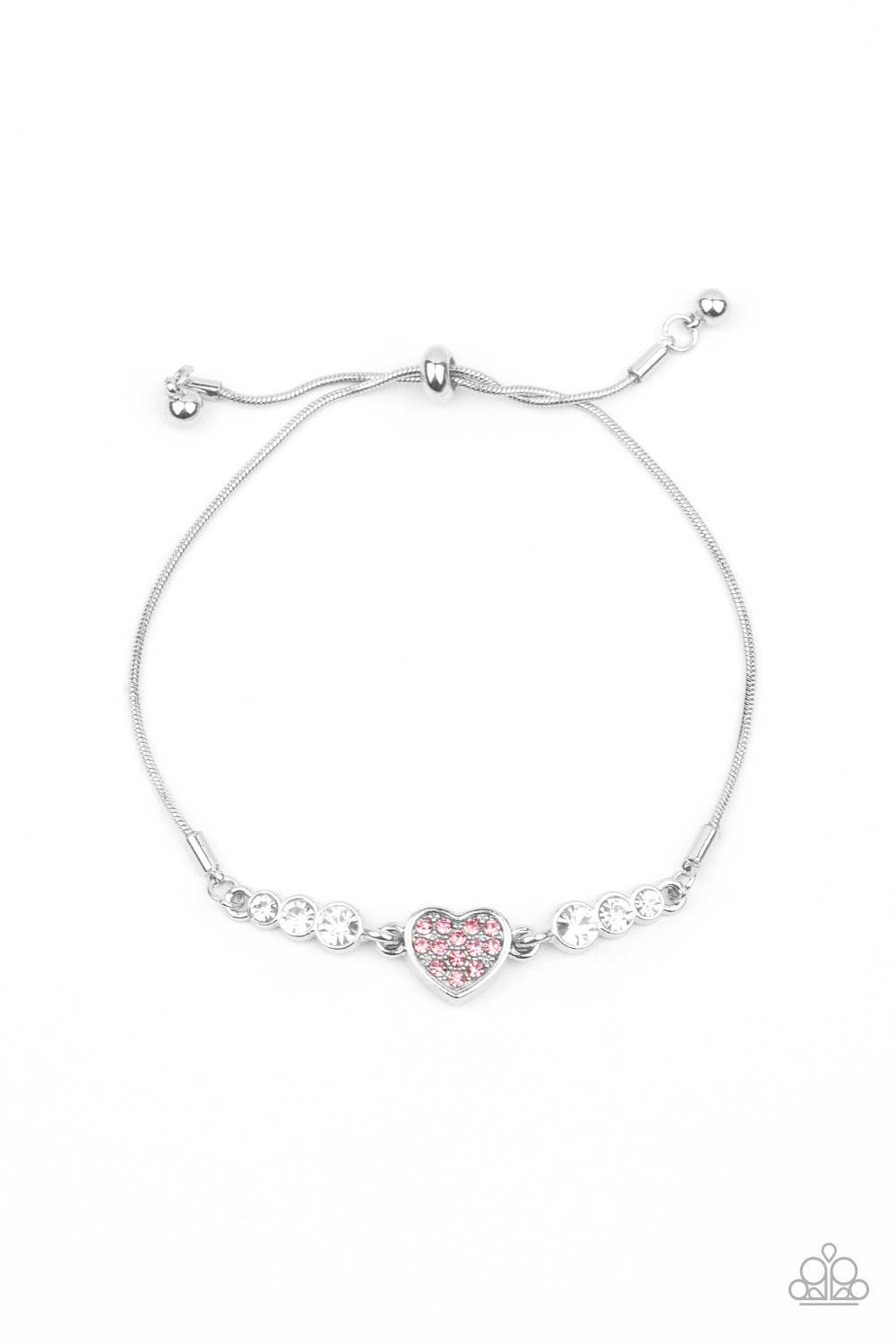 Paparazzi Accessories Big-Hearted Beam - Pink A trio of glassy white rhinestones flank a shiny silver heart charm, creating a flirty centerpiece. Glittery pink rhinestones dot the dainty heart, adding a splash of color to the glittery display. Features an