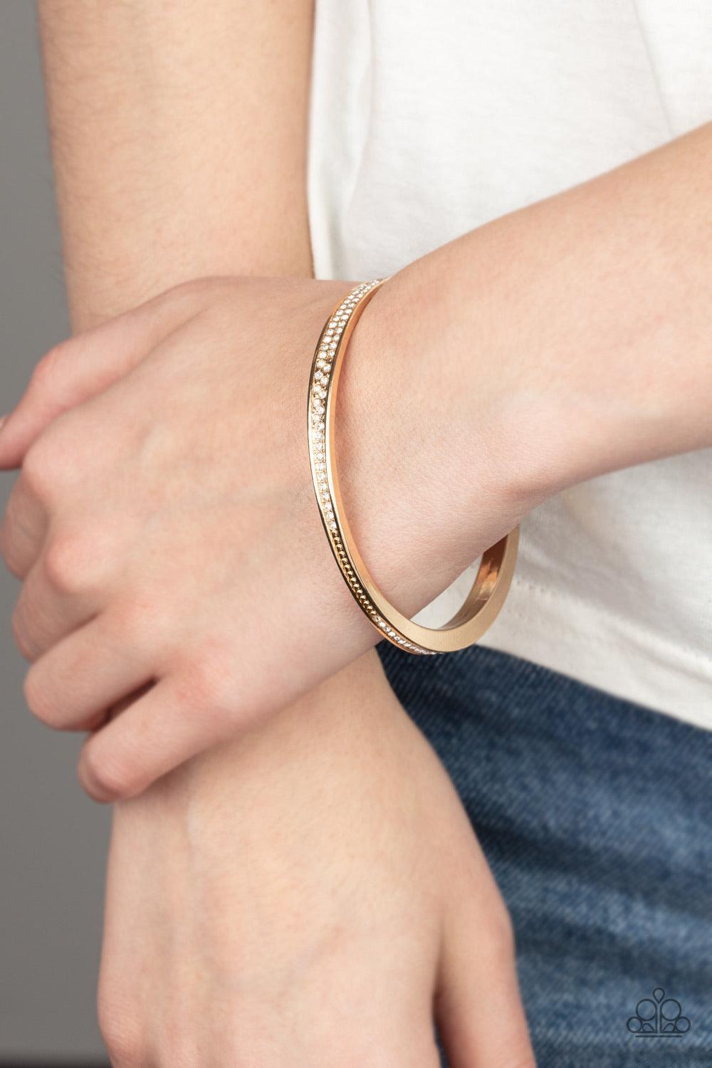 Paparazzi Accessories Power Move - Gold Rows of dainty white rhinestones have been encrusted along the front of a thick asymmetrical gold bangle for a timeless twist. Sold as one individual bracelet. Jewelry