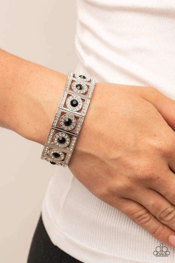 Paparazzi Accessories Ultra Upscale - Black A glassy black rhinestone is pressed into a ring of glitzy white rhinestones inside a rectangular silver frame dusted in dazzling white rhinestones. The timeless frames sparkle along stretchy bands around the wr