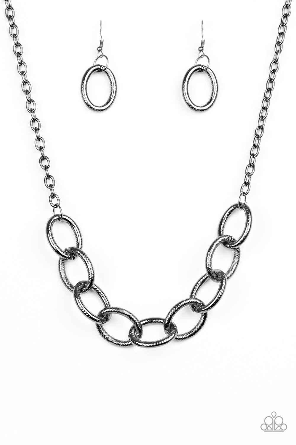 Paparazzi Accessories Boldly Bronx - Black Features bold gunmetal links that connect below the collar for a dramatic industrial look. Features an adjustable clasp closure. Sold as one individual necklace. Includes one pair of matching earrings. Jewelry