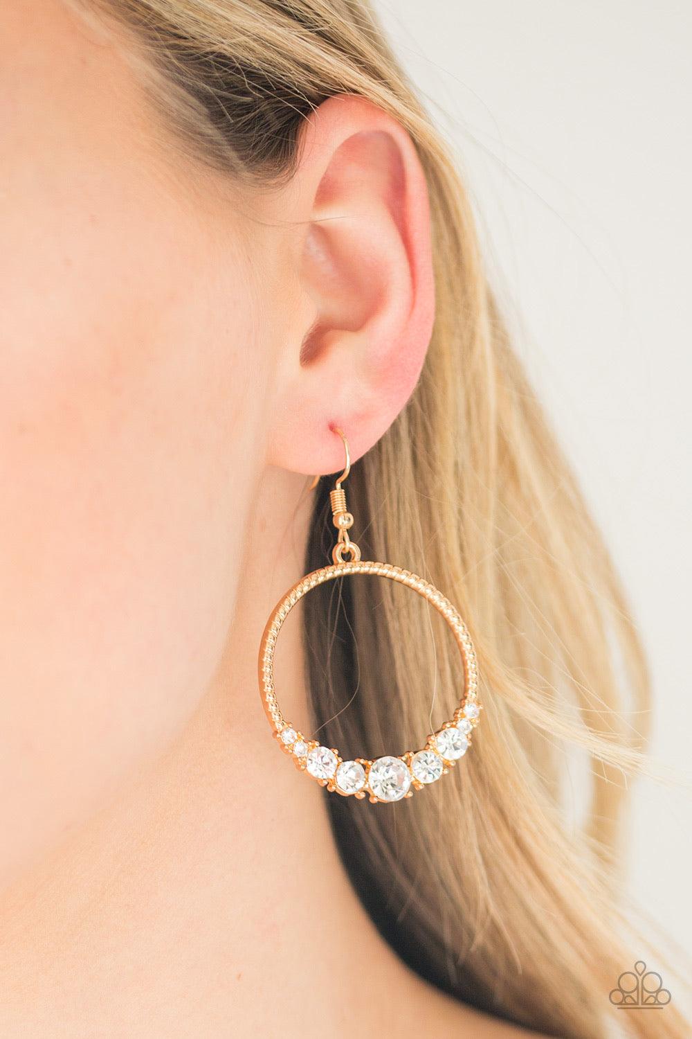 Paparazzi Accessories Self-Made Millionaire - Gold The bottom of a textured gold hoop is encrusted in glittery white rhinestones for a glamorous look. Earring attaches to a standard fishhook fitting. Sold as one pair of earrings. Jewelry