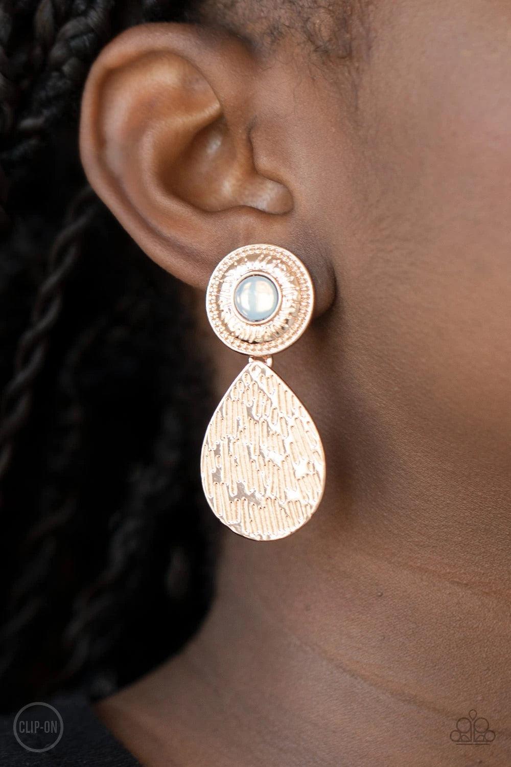 Paparazzi Accessories Emblazoned Edge - Rose Gold *Clip-On A hammered rose gold teardrop dangles from the bottom of an ornate rose gold disc that is dotted with a dreamy opal beaded center. Earring attaches to a standard clip-on fitting. Sold as one pair
