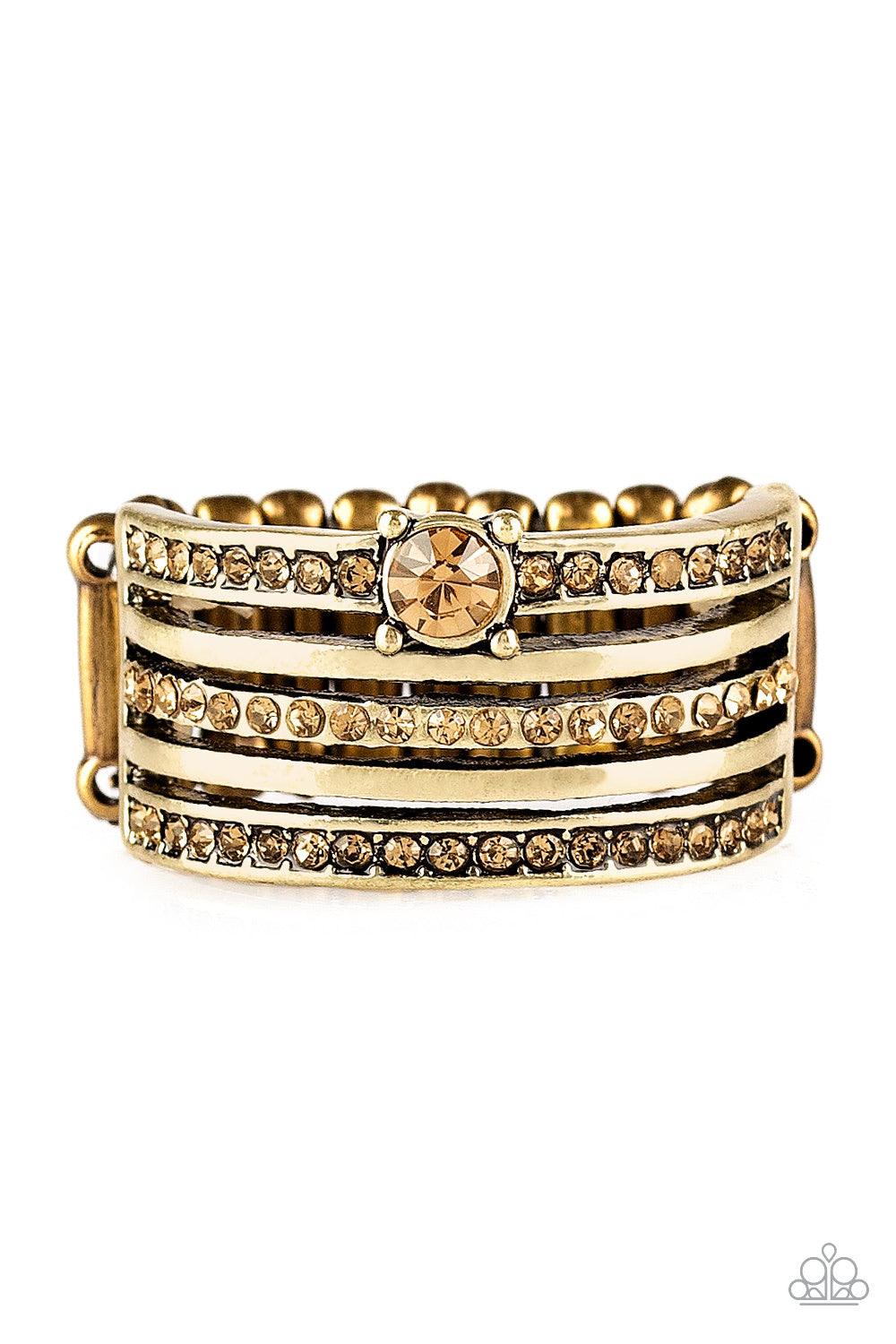 Paparazzi Accessories The Dealmaker - Brass Encrusted in golden topaz rhinestones, glittery bands alternate with shiny brass bands across the finger. A slightly larger rhinestone adorns the uppermost band for a refined finish. Features a stretchy band for