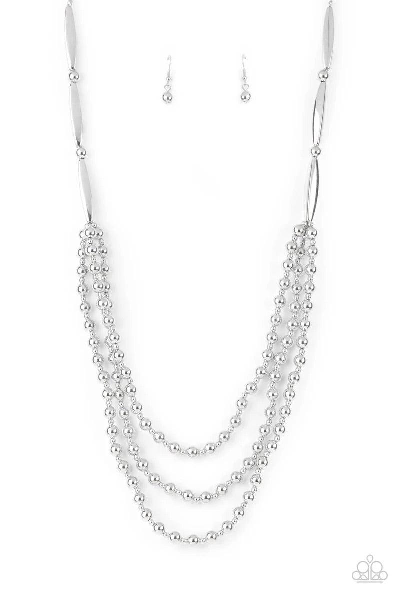Paparazzi Accessories Beaded Beacon - Silver Brushed in a shiny shimmer, dainty and classic silver beads alternate across the chest in three gleaming layers. The tiered display attaches to oblong and classic silver beads that connect to a silver chain for