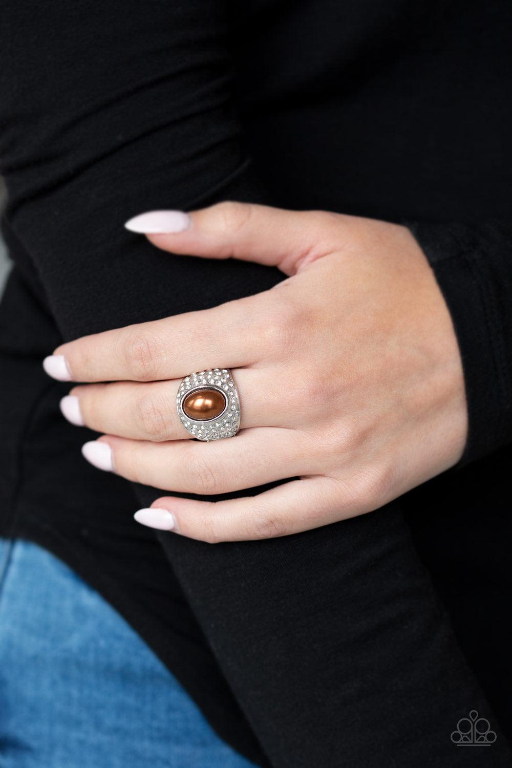 Paparazzi Accessories Glittering Go-Getter - Brown A pearly brown bead is pressed into the center of a bold silver band radiating with countless white rhinestones, creating a dramatic statement piece atop the finger. Features a stretchy band for a flexibl