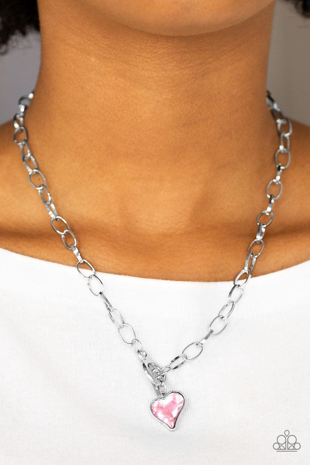 Paparazzi Accessories Princeton Princess - Pink Cut into a whimsical heart shape, a glittery pink gem swings from the bottom of a glistening silver chain below the collar for a charming look. Features a toggle closure. Jewelry