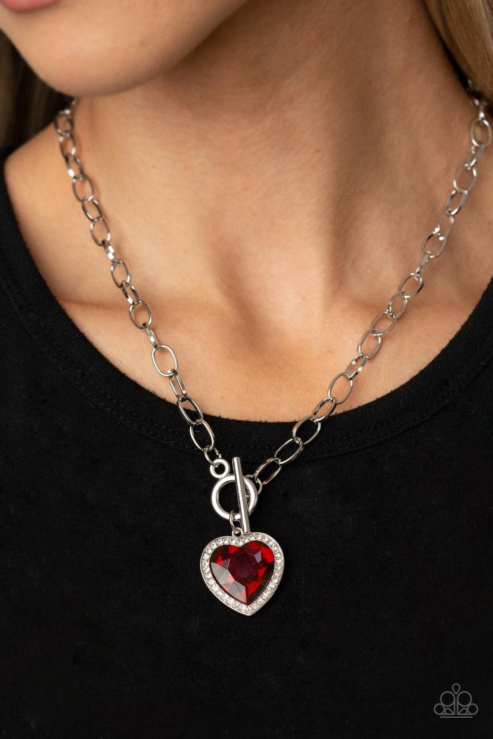 Paparazzi Accessories Check Your Heart Rate - Red Bordered in glassy white rhinestones, a heart-shaped red gem is pressed into a shiny silver pendant at the bottom of a bold silver chain below the collar for a flirtatious finish. Features a toggle closure
