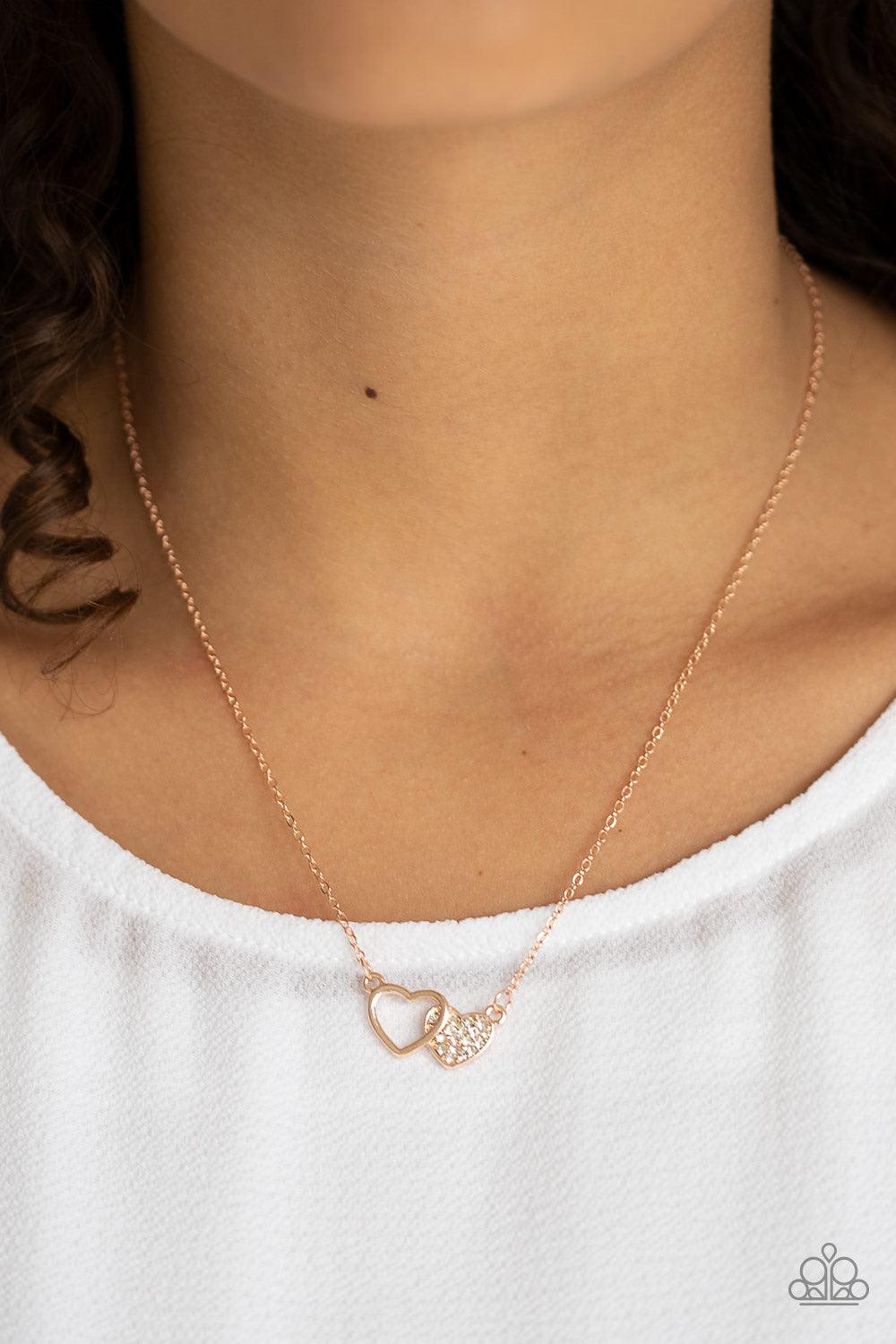 Paparazzi Accessories Charming Couple - Rose Gold A white rhinestone encrusted rose gold heart joins a glistening rose gold heart silhouette at the bottom of a shimmery rose gold chain, creating a charming pendant below the collar. Features an adjustable