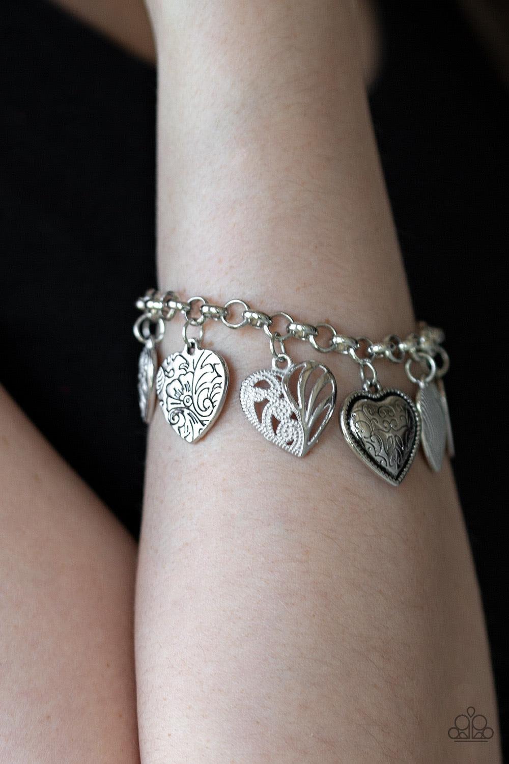 Paparazzi Accessories Garden Hearts - White Featuring an array of floral patterns, a collection of silver hearts swing from a shimmery silver chain. Alternating charms are brushed in a shiny white finish, creating a colorful fringe around the wrist. Featu