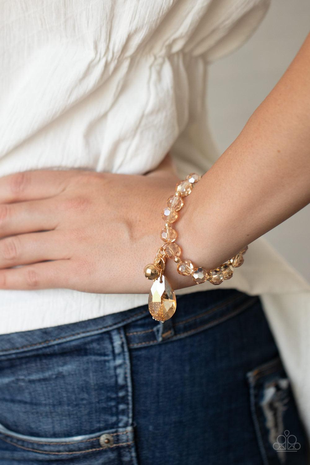 Paparazzi Accessories Leaving So SWOON? - Gold A collection of dainty gold beads and golden faceted crystal-like beads are threaded along stretchy bands around the wrist. A classic gold bead, golden teardrop crystal, and gold chain tassel swing from a gli
