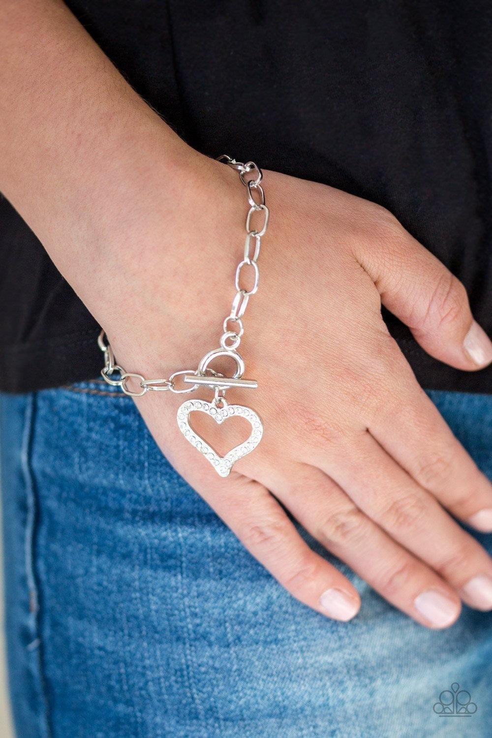 Paparazzi Accessories March to a Different HEARTBEAT - White Encrusted in glassy white rhinestones, a glittery silver heart charm swings from a glistening silver chain for a flirtatious look. Features a toggle closure. Sold as one individual bracelet. Jew