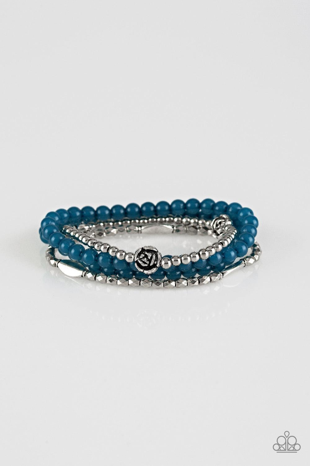 Paparazzi Accessories Blooming Buttercups - Blue Mismatched silver beads and strands of glassy blue beads are threaded along stretchy bands. Infused with silver accents, dainty rose blossoms adorn the wrist for a seasonal finish. Sold as one set of four b