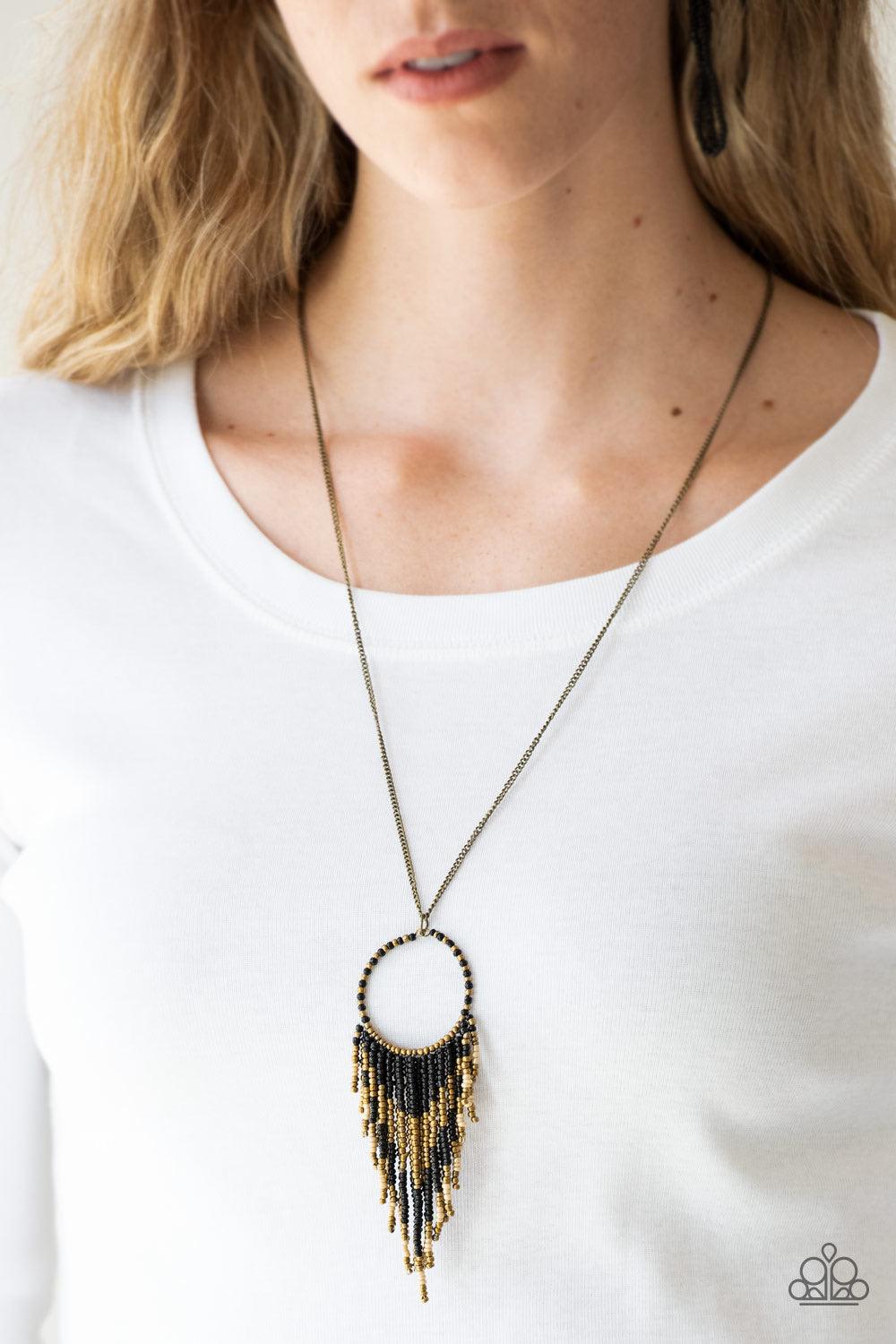 Paparazzi Accessories Badlands Beauty - Black Infused with black, brass, and brown seed beads, a colorful dream catcher like pendant swings from the bottom of a lengthened brass chain for a tribal inspired look. Features an adjustable clasp closure. Sold