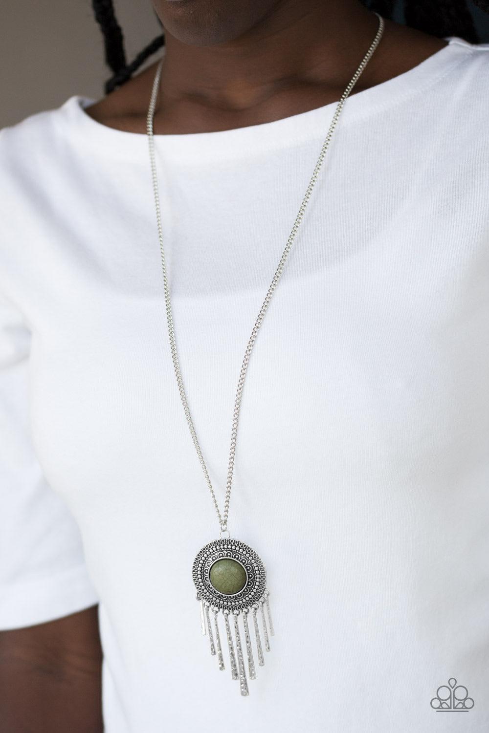 Paparazzi Accessories Bon Voyager - Green An earthy green stone is pressed into the center of a shimmery silver disc radiating with glistening tribal details. Swinging from the bottom of a lengthened silver chain, the bold pendant gives way to a fringe of