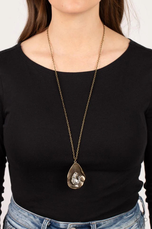 Paparazzi Accessories Surrealist Sparkle - Brass A warped brass frame gently folds around an oversized white teardrop gem center, resulting in a gritty yet glamorous pendant at the bottom of a lengthened brass chain. Features an adjustable clasp closure.